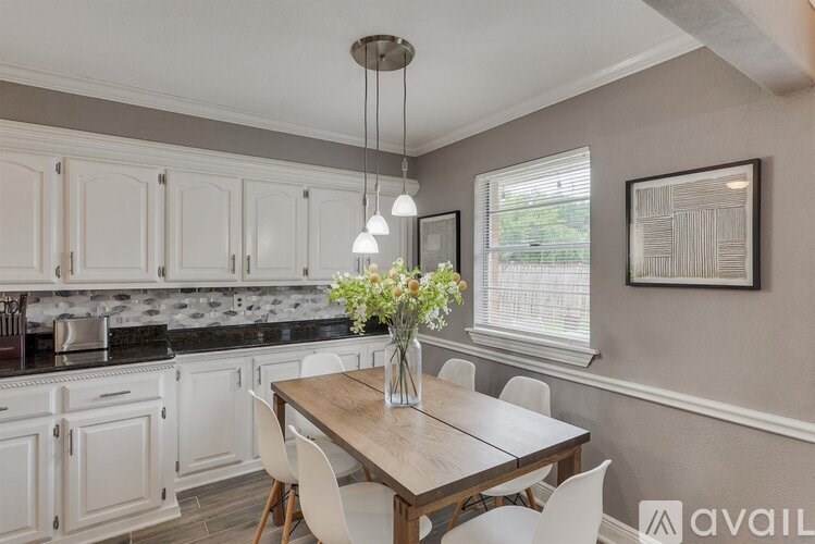 A kitchen with a table and chairs and a vase of flowers on the table.