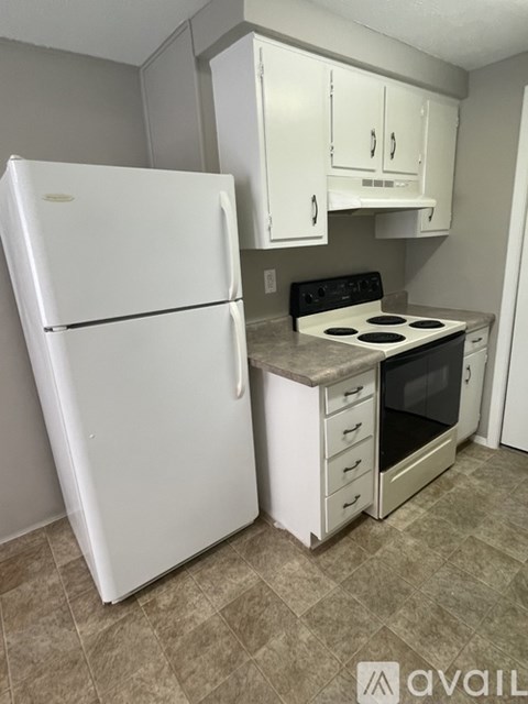 A white refrigerator stands in a kitchen with a stove and white cabinets.