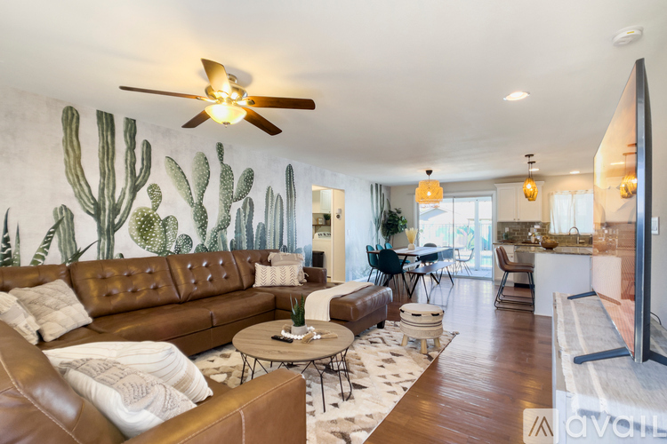 A living room with a brown leather couch and a cactus mural on the wall.