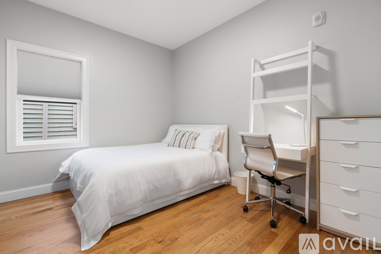A white bedroom with a bed, chair, and drawers.