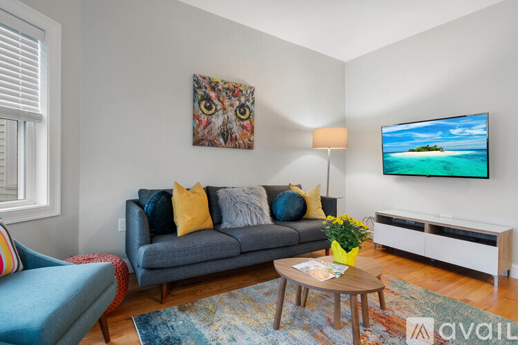 A living room with a grey couch, a coffee table, a TV, and a painting of an owl on the wall.