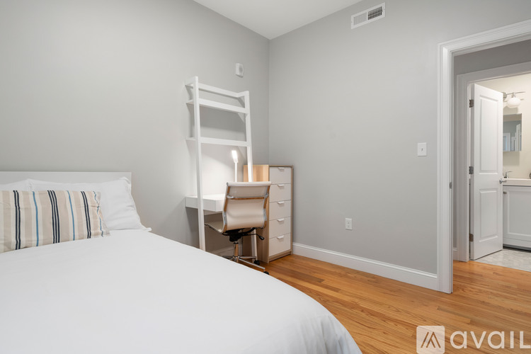 A bedroom with a white bed and a wooden dresser.