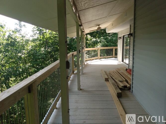 A wooden deck with a railing and a bench is surrounded by greenery.