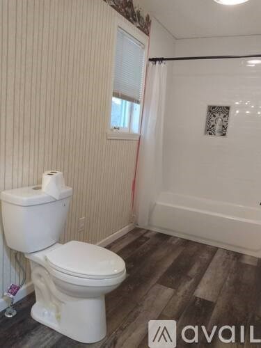 A white toilet in a bathroom with wooden flooring and a white bathtub.