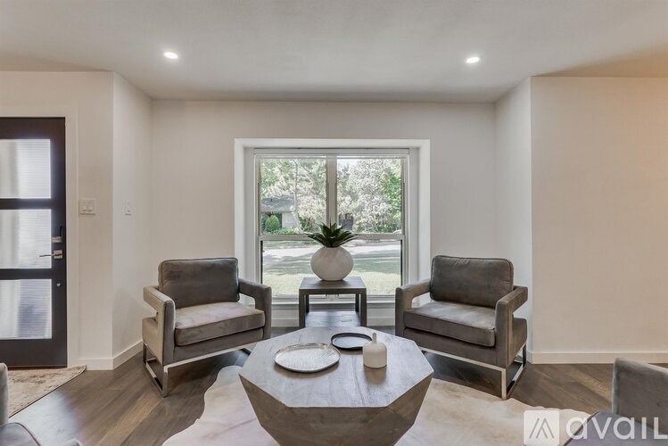 A living room with a large window, two grey armchairs, and a coffee table.