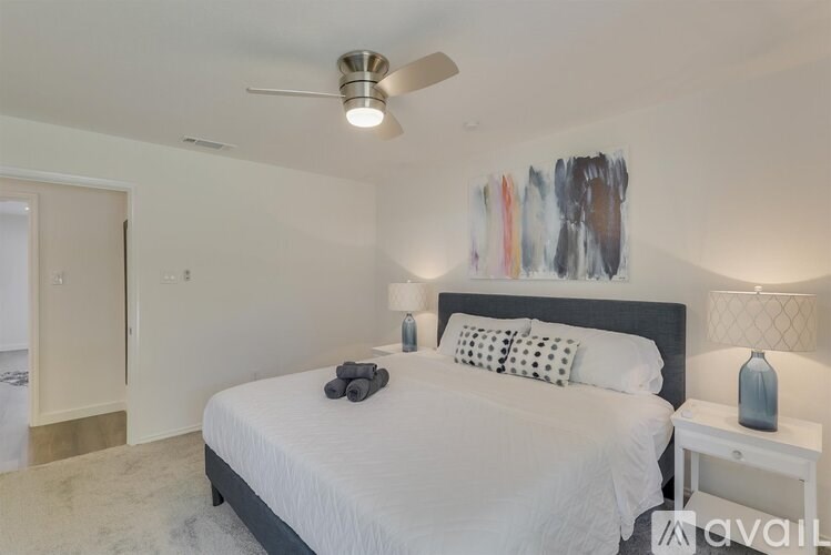 A bedroom with a large bed, a ceiling fan, and a painting on the wall.