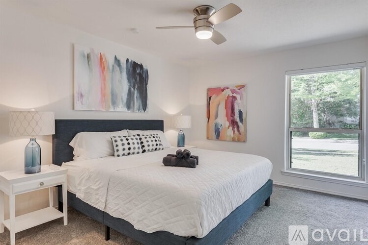 A bedroom with a large bed, a ceiling fan, and two paintings on the wall.