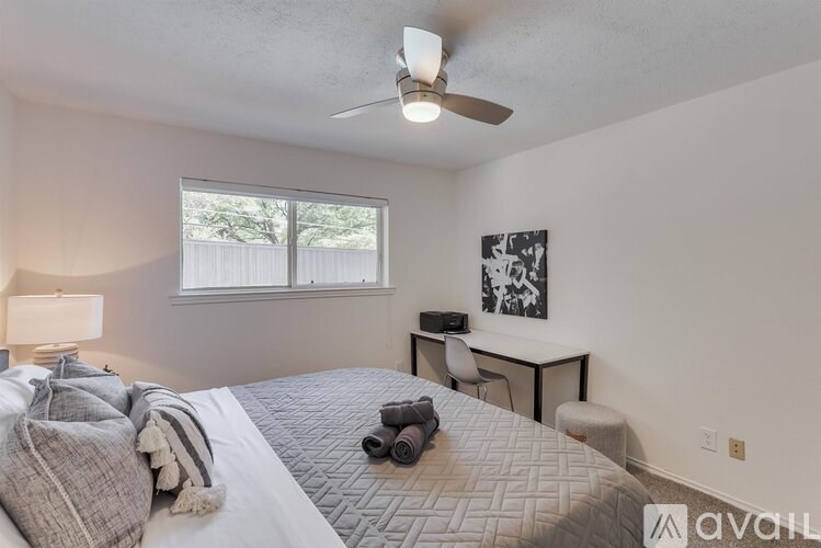 A bedroom with a bed, desk, chair, and a ceiling fan.