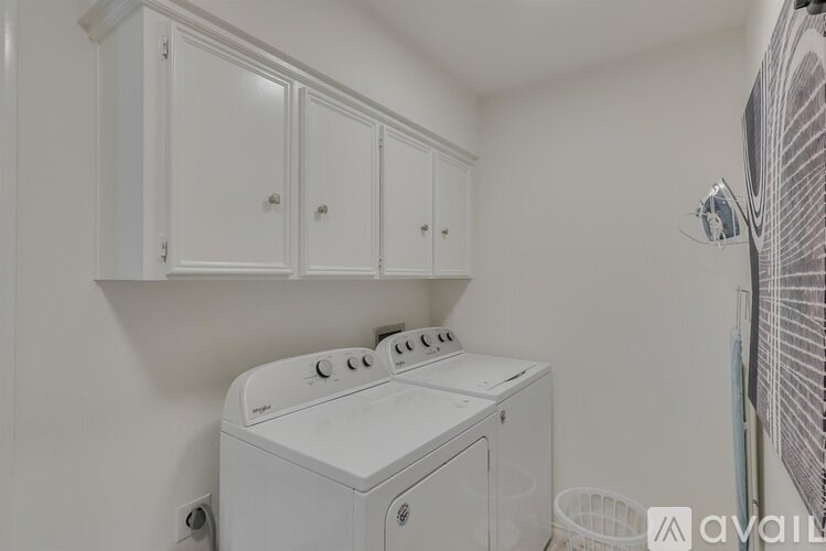 A white washing machine sits in a laundry room with white cabinets above it.