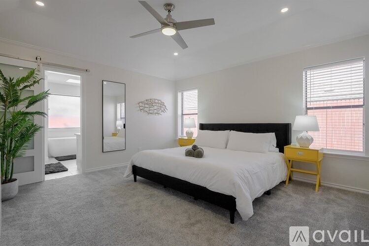 A bedroom with a large bed, a ceiling fan, and a potted plant.