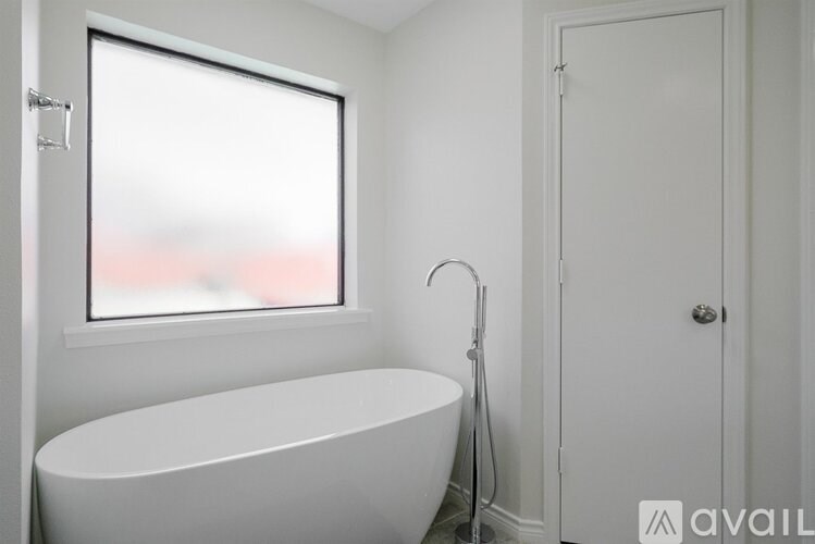 A white bathroom with a tub, shower head, and a window.