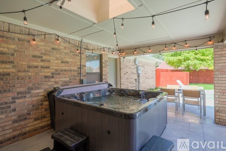 A hot tub is in the middle of a patio with lights strung above it.