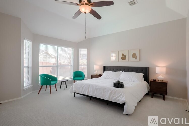 A bedroom with a large bed, a ceiling fan, and two chairs.