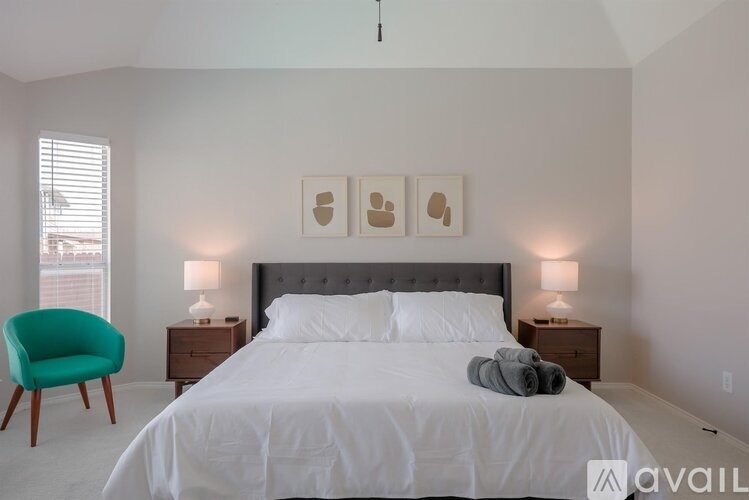 A bedroom with a large bed, a green chair, and two lamps.