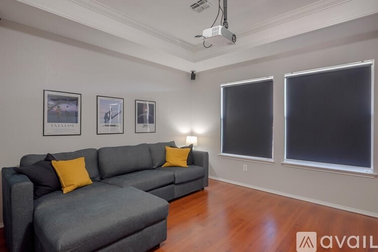 A grey couch with yellow pillows in a room with a white wall and a window.