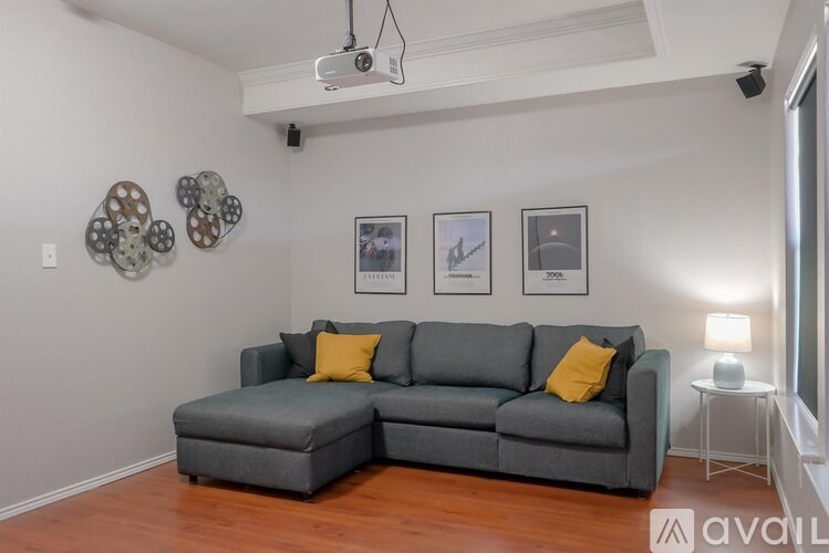 A grey sectional sofa with a yellow pillow is in the center of a room with a white wall and a picture frame.