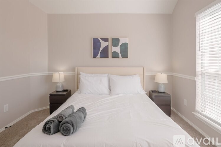 A bedroom with a large bed, two lamps, and a painting on the wall.