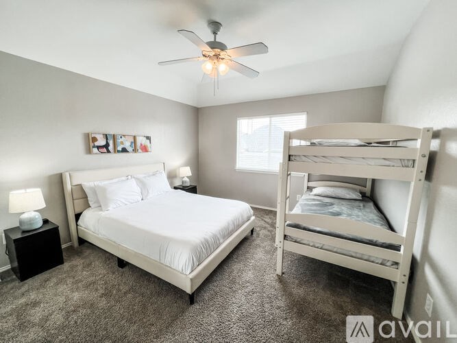A bedroom with a white bed and a bunk bed with a ceiling fan.
