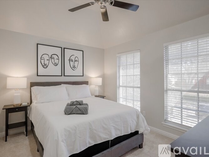 A bedroom with a bed, two lamps, a ceiling fan, and two framed pictures on the wall.