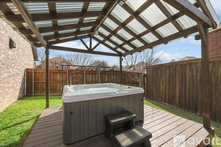 A hot tub is under a wooden pergola in a backyard.