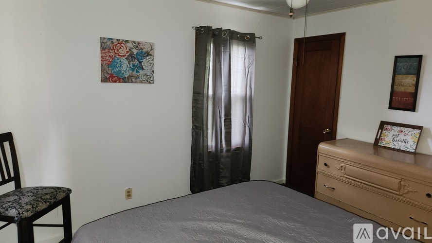 A bedroom with a bed, chair, and two pictures on the wall.