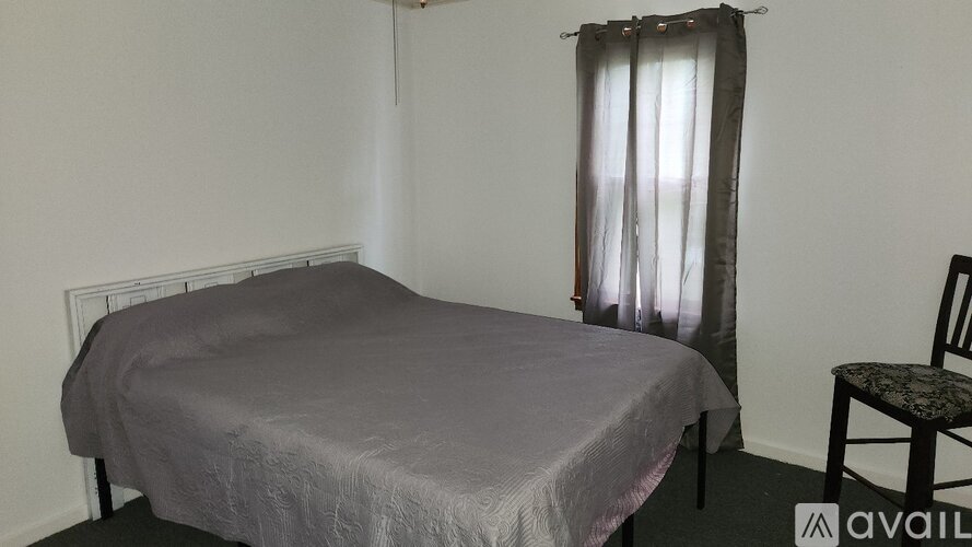 A bedroom with a bed, chair, and window with curtains.