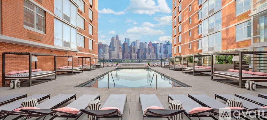 A pool area with sun loungers and a view of a city skyline.
