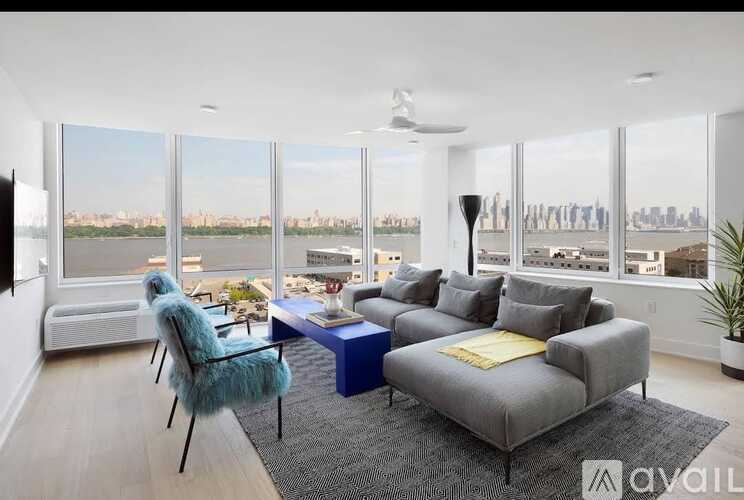 A living room with a grey couch, a blue table, and a large window with a view of the city.
