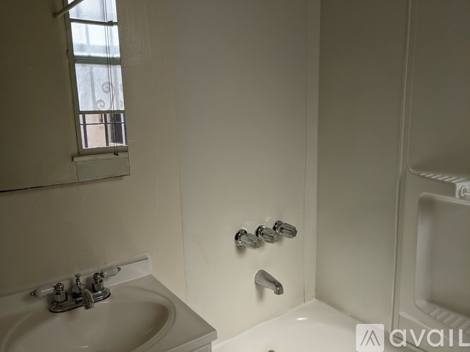 A white bathroom with a sink, tub, and window.