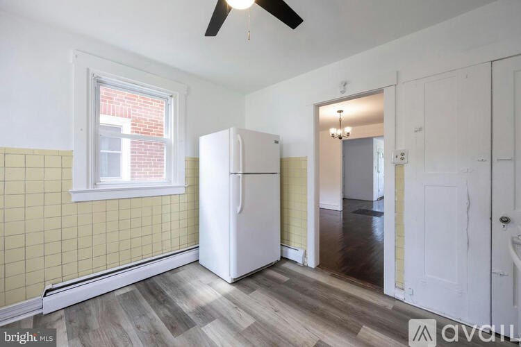 A room with a white fridge and a window with yellow tiles on the wall.