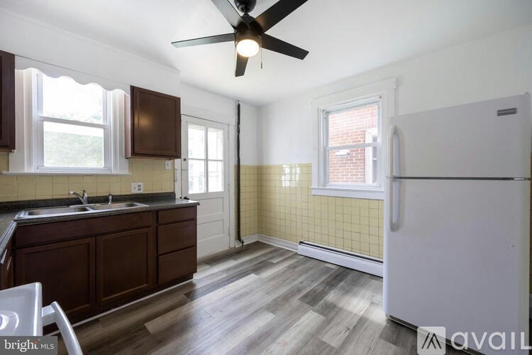 A kitchen with a white fridge, wooden floors and a ceiling fan.