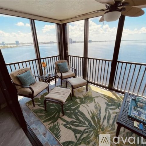 A balcony with a table, chairs, and a ceiling fan overlooking a body of water.