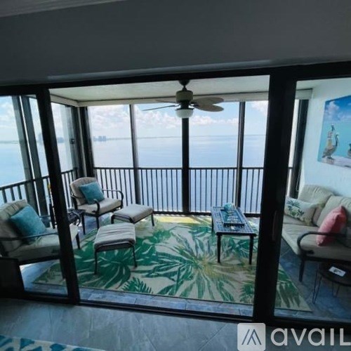 A balcony with a fan, chairs, and a couch overlooking the water.