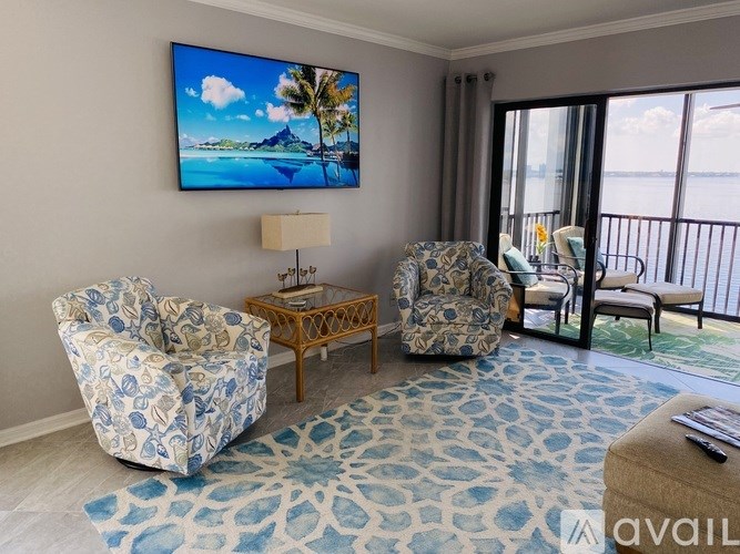 A living room with a large screen TV and a view of the ocean.