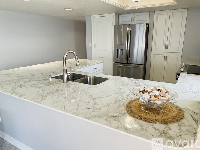 A kitchen with a marble countertop and a stainless steel refrigerator.