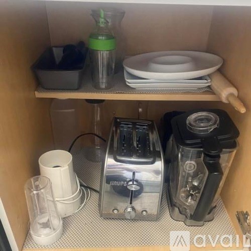 A kitchen appliance is on a shelf with a green bottle and a white container.