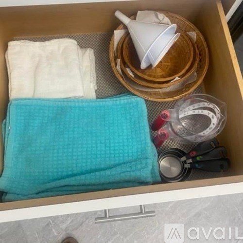 A drawer contains a blue towel, a white plastic container, a wooden bowl, and a measuring tape.