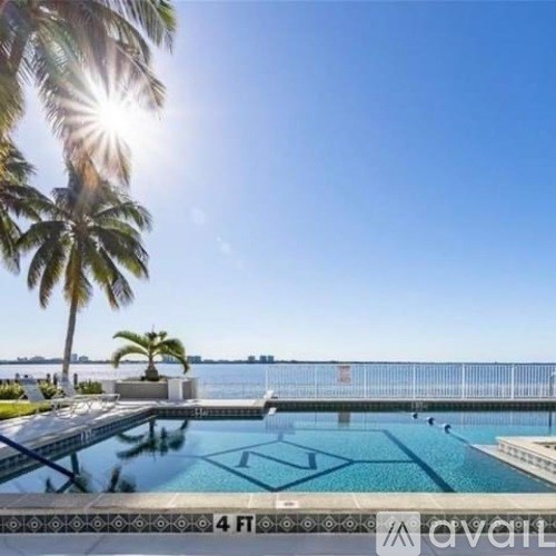 A pool surrounded by palm trees with the sun shining brightly.