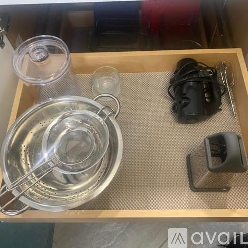 A wooden drawer with a metal bowl, a glass, a black object, and a black bag.
