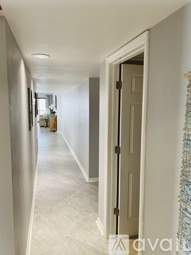 A hallway with a white door and a wall hanging on the right.
