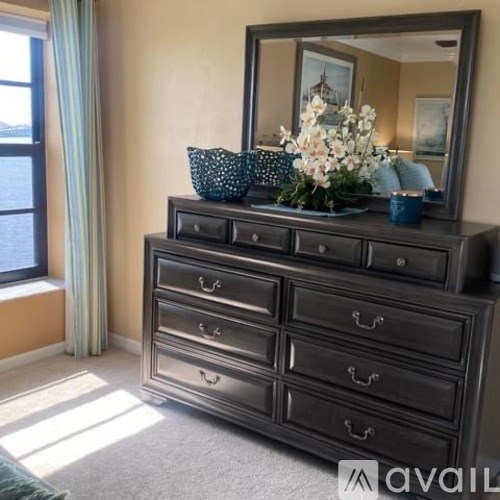 A large mirror is on top of a dresser with a vase of flowers and a pillow on it.