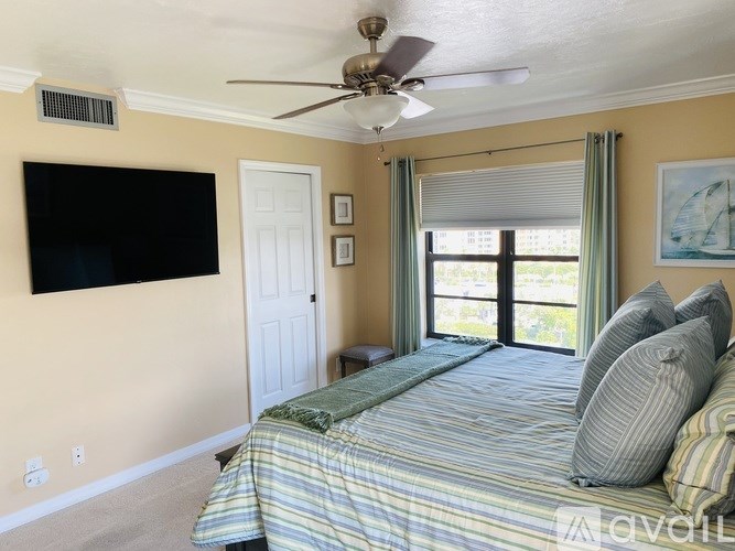 A bedroom with a bed, a ceiling fan, and a flat-screen TV mounted on the wall.