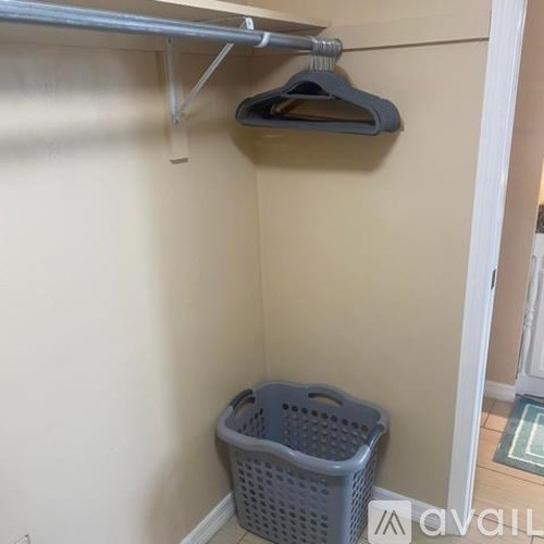 A grey plastic laundry basket sits under a clothes rack.