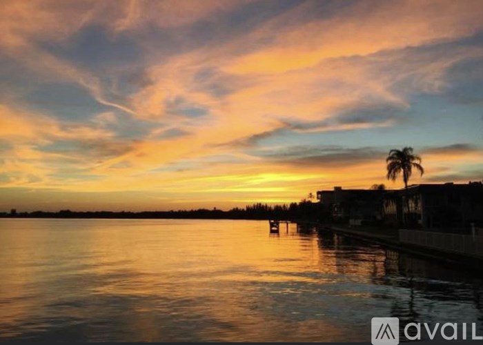 A beautiful sunset over a calm body of water with palm trees in the distance.