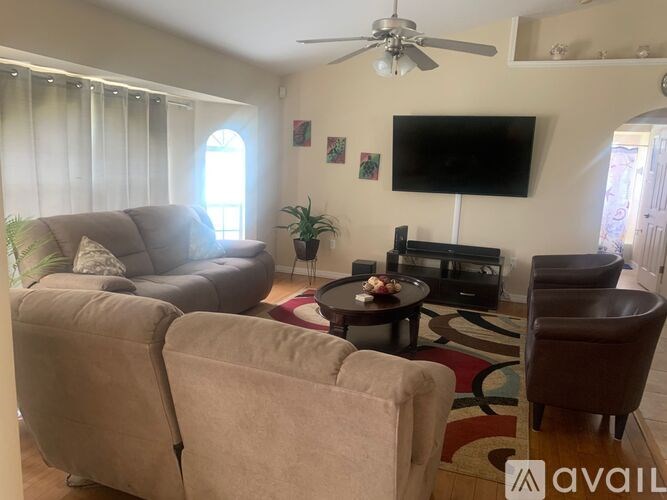 A living room with a grey couch, a brown chair, a black television and a ceiling fan.
