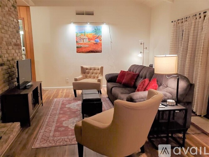 A living room with a grey couch, a brown chair, a red cushion, a television, a rug, a lamp, and a painting on the wall.