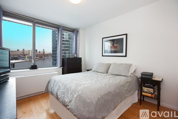 A bedroom with a large bed, a window with a view of the city, and a picture frame on the wall.