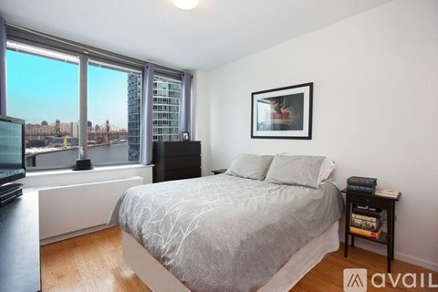 A bedroom with a large bed, a window with a view of the city, and a picture frame on the wall.
