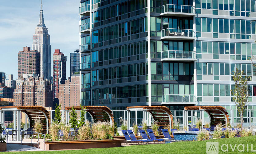 A modern building with a pool and lounge chairs in the foreground and the Empire State Building in the background.