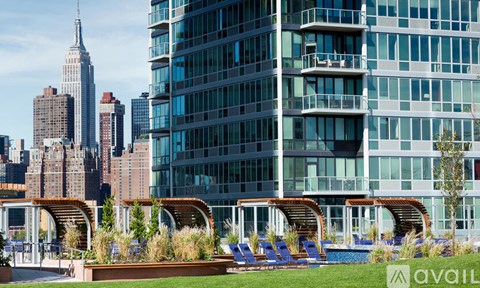 A modern building with a pool and lounge chairs in the foreground and the Empire State Building in the background.